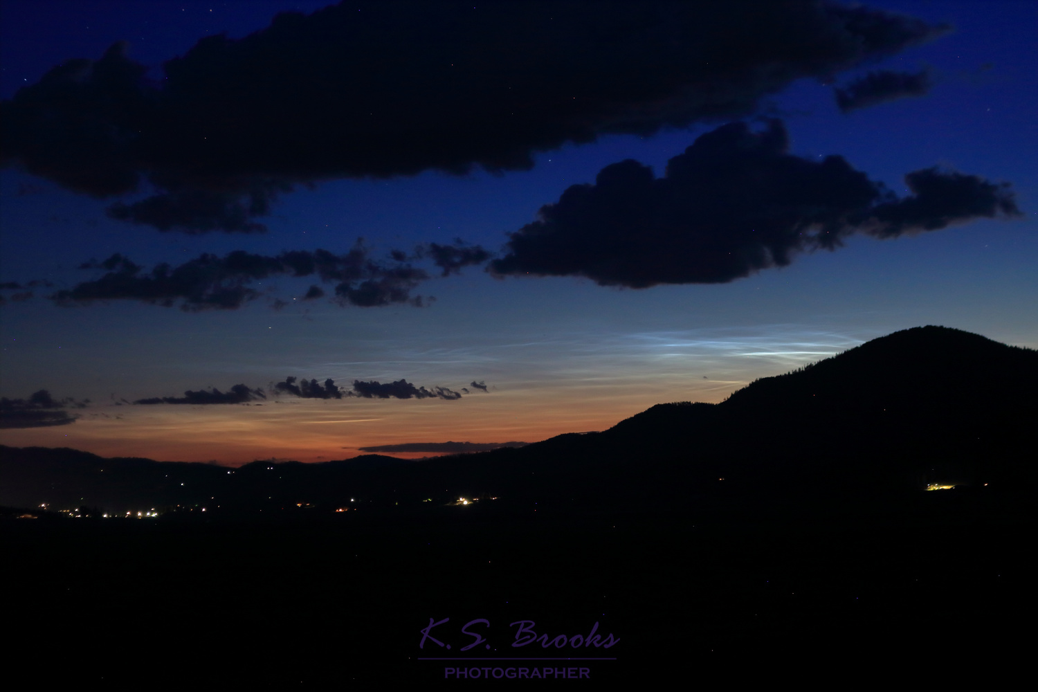 Noctilucent clouds at sunrise next to mountains over a small town. photo by KS Brooks